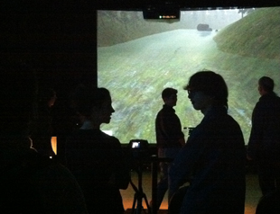 Photo of students in a dark room standing in front of a projector showing gameplay